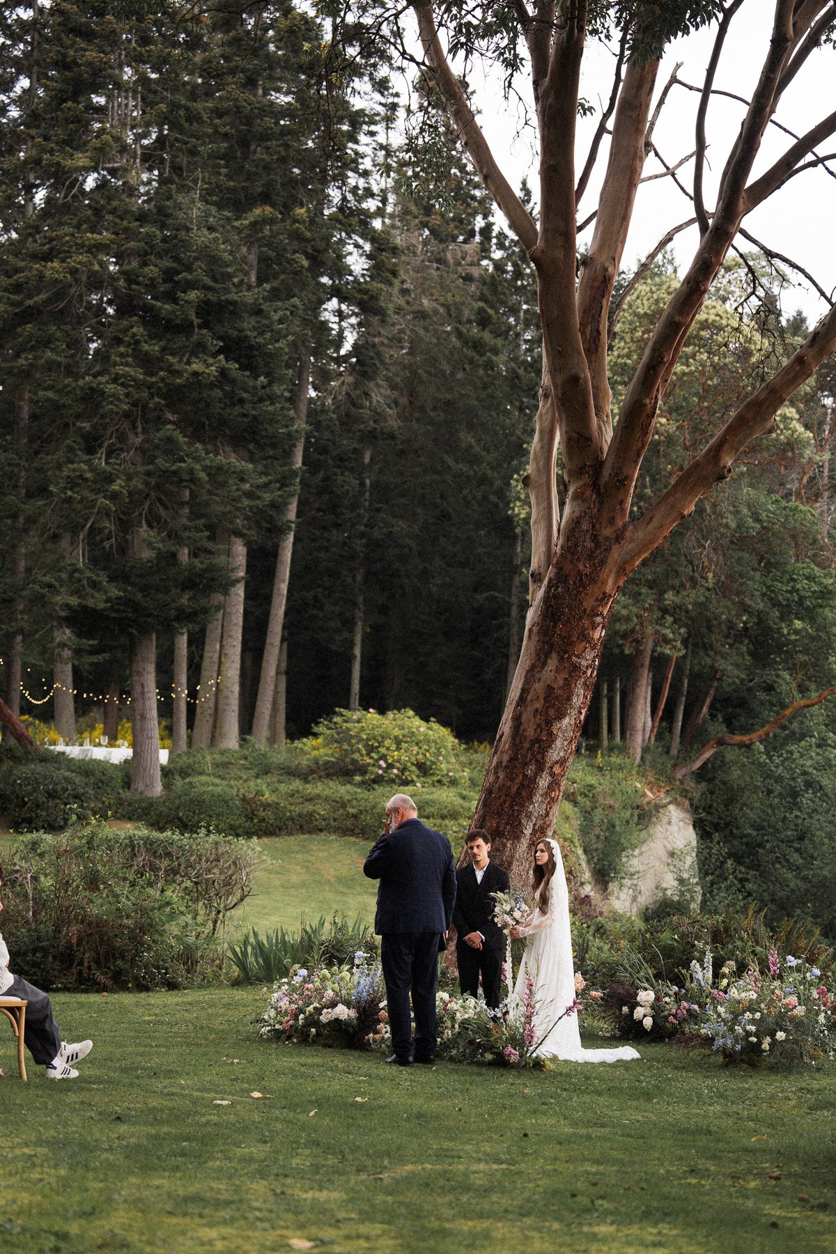 Bride and groom standing beneath a tree during an outdoor wedding ceremony