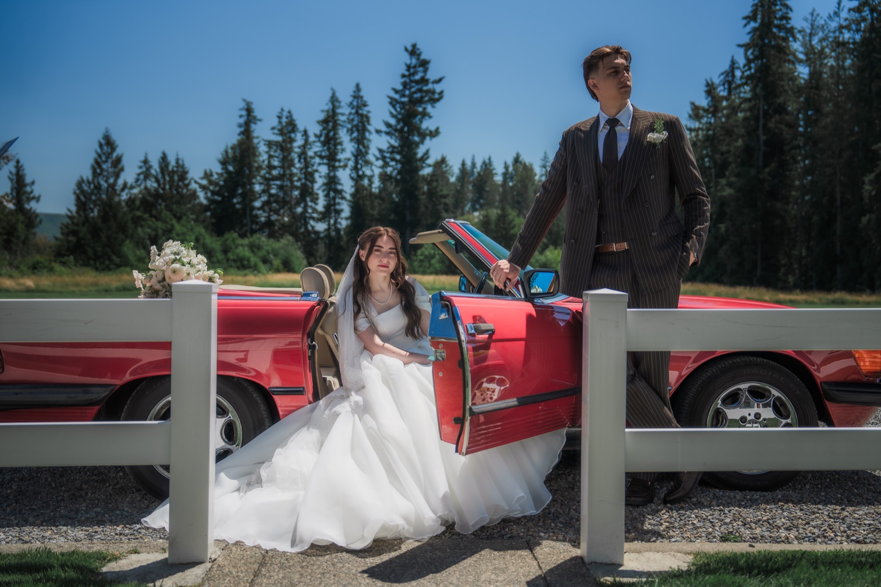 Newlyweds beside a red classic convertible